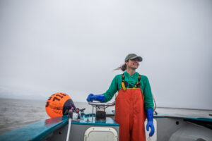 Female salmon harvester driving boat smiles in Prince William Sound, Alaska.