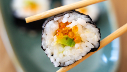Pair of chopsticks holding maki sushi with Alaska Salmon Roe and Avocado.