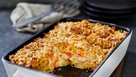 Baked mac 'n' cheese with fresh Alaska Surimi in a casserole dish with servings scooped out of the dish.